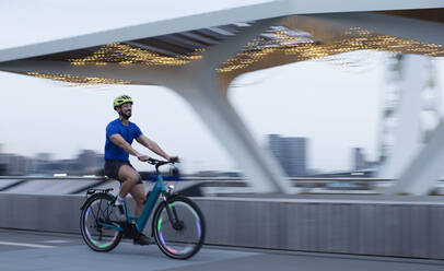 Man riding illuminated bicycle along city waterfront, London, UK - CAIF31905