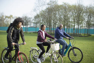 Father and teen kids riding bicycles in park grass - CAIF31908