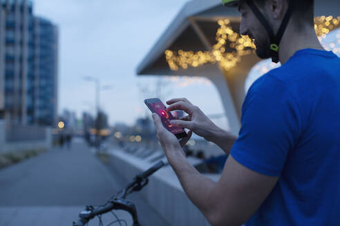 Mann auf dem Fahrrad, der in der Stadt die Herzfrequenz auf einer Smartphone-App anzeigt - CAIF31936