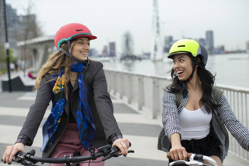 Glückliche junge Frauen Freunde in Helmen fahren Fahrräder in der Stadt - CAIF31949