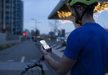 Mann auf dem Fahrrad in der nächtlichen Stadt beim Videochatten mit dem Smartphone - CAIF31950
