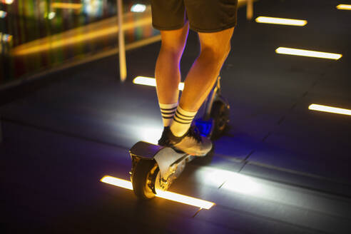 Man riding scooter on illuminated sidewalk at night - CAIF31965