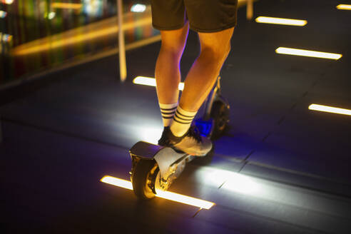 Mann fährt Roller auf beleuchtetem Gehweg bei Nacht - CAIF31965