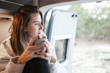 Thoughtful woman sitting inside camper van - MRRF01786