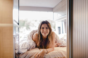 Beautiful woman lying on bed in camper van - MRRF01788