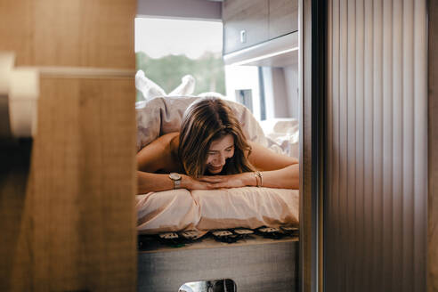 Fröhliche Frau entspannt sich auf dem Bett im Wohnmobil - MRRF01789
