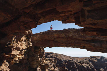 Man standing on natural rock arch in Gran Canaria, Spain - RSGF00748