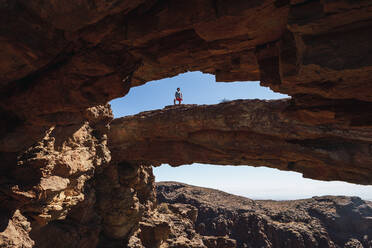 Mann steht auf einem natürlichen Felsbogen auf Gran Canaria, Spanien - RSGF00748
