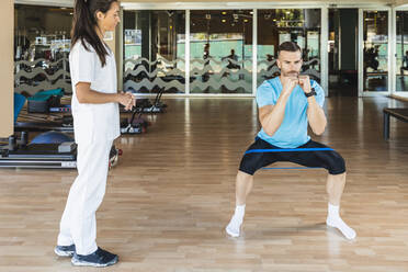 Fitness-Lehrer betrachtet Sportler, der mit einem Widerstandsband im Fitnessstudio trainiert - IFRF01270