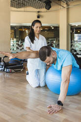 Athlete exercising on sports ball in gym - IFRF01278