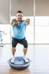 Sportler in der Hocke auf dem Balanceball im Fitnessstudio - IFRF01282