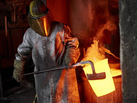 Gießereiarbeiter trägt brennenden Behälter mit Handwerkzeug in der Industrie - CVF01766