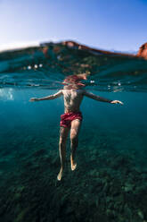 Man wearing trunks swimming in sea - RSGF00750