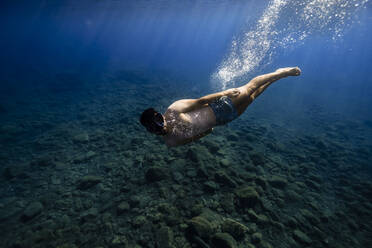 Junger Mann mit Schwimmbrille schwimmt unter Wasser - RSGF00751