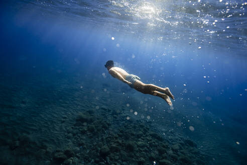 Hemdloser junger Mann schwimmt unter Wasser - RSGF00753