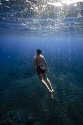 Hemdloser junger Mann schwimmt unter Wasser im Meer - RSGF00754