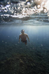 Young man with goggles swimming underwater - RSGF00757