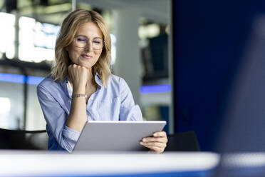 Lächelnde Geschäftsfrau mit Hand am Kinn, die einen Tablet-PC im Büro benutzt - PESF03351