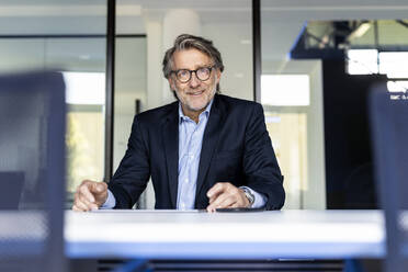 Smiling businessman with eyeglasses at office desk - PESF03353