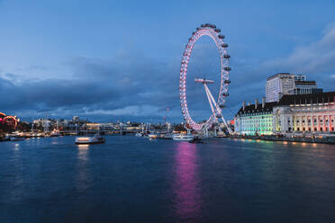 Illuminated Millennium Wheel by Thames riverbank in city at dusk, London, England, UK - MRRF01796