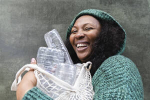 Happy woman holding plastic water bottles in mesh bag - ASGF01958