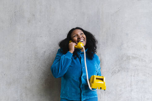 Glückliche Frau spricht am Retro-Telefon vor einer grauen Wand - ASGF01960