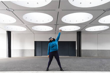 Woman raising hand wearing VR headset under illuminated ceiling - ASGF01966