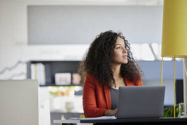 Contemplative businesswoman with laptop at desk in office - RBF08458