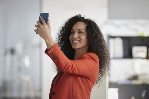 Lächelnde Geschäftsfrau nimmt Selfie durch Smartphone am Arbeitsplatz - RBF08468