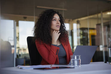 Contemplative businesswoman sitting with hand on chin in office - RBF08473
