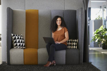 Geschäftsfrau sitzt mit Laptop auf dem Sofa im Büro - RBF08508