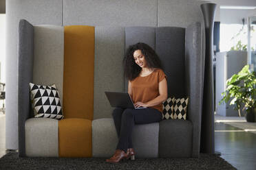 Smiling businesswoman working using laptop on sofa in office - RBF08510