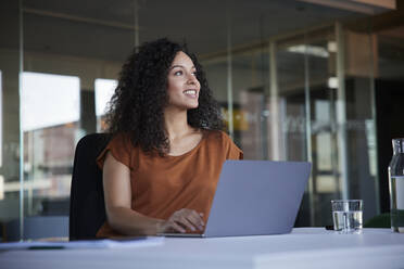 Glückliche Geschäftsfrau mit Laptop auf dem Schreibtisch träumt Tag im Büro - RBF08515