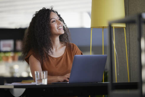 Glückliche Geschäftsfrau mit Laptop auf dem Schreibtisch träumt am Arbeitsplatz - RBF08519