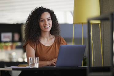 Smiling businesswoman with laptop on desk at workplace - RBF08520