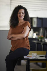 Smiling businesswoman sitting with arms crossed on desk in office - RBF08521