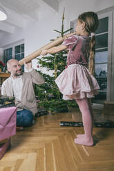 Vater betrachtet Tochter durch aufgerolltes Geschenkpapier zu Hause - KMKF01783