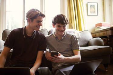 Glückliche Teenager mit Laptops, die im Wohnzimmer lernen - CAIF31971