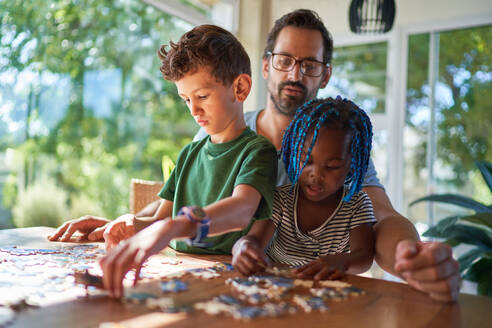 Father and kids assembling jigsaw puzzle at home - CAIF31986