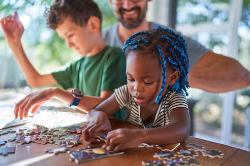 Cute toddler girl assembling jigsaw puzzle with family at table - CAIF31992