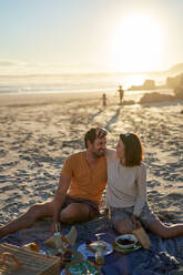 Happy affectionate couple enjoying picnic on sunny beach - CAIF31998