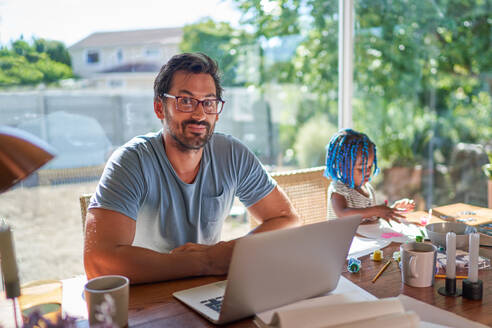 Porträt Vater arbeitet am Laptop neben der Tochter, die mit dem Finger malt - CAIF32001