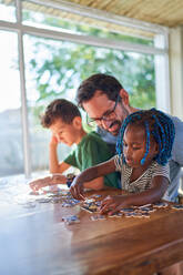 Vater und Kinder beim Zusammensetzen eines Puzzles am Esstisch - CAIF32003
