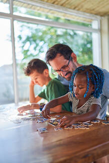 Father and kids assembling jigsaw puzzle at dining table - CAIF32003