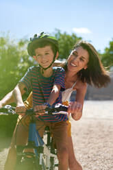 Glückliche Mutter mit Sohn beim Fahrradfahren in einer sonnigen Einfahrt - CAIF32011