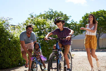 Glückliche Familie beim Fahrradfahren in sonniger Einfahrt - CAIF32013