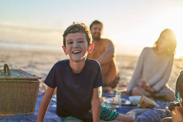 Portrait cute boy with sandy face on sunny beach with family - CAIF32017