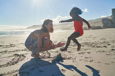 Mother and playful toddler daughter on sunny summer beach - CAIF32023