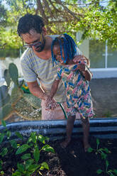 Father and toddler daughter watering plants in garden - CAIF32030