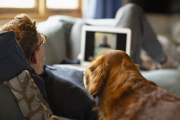 Mann mit Hund beim Videochat mit Laptop auf dem Sofa - CAIF32050